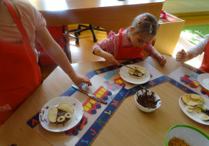 Dzieci układają kawałki owoców na waflu posmarowanym czekoladą.